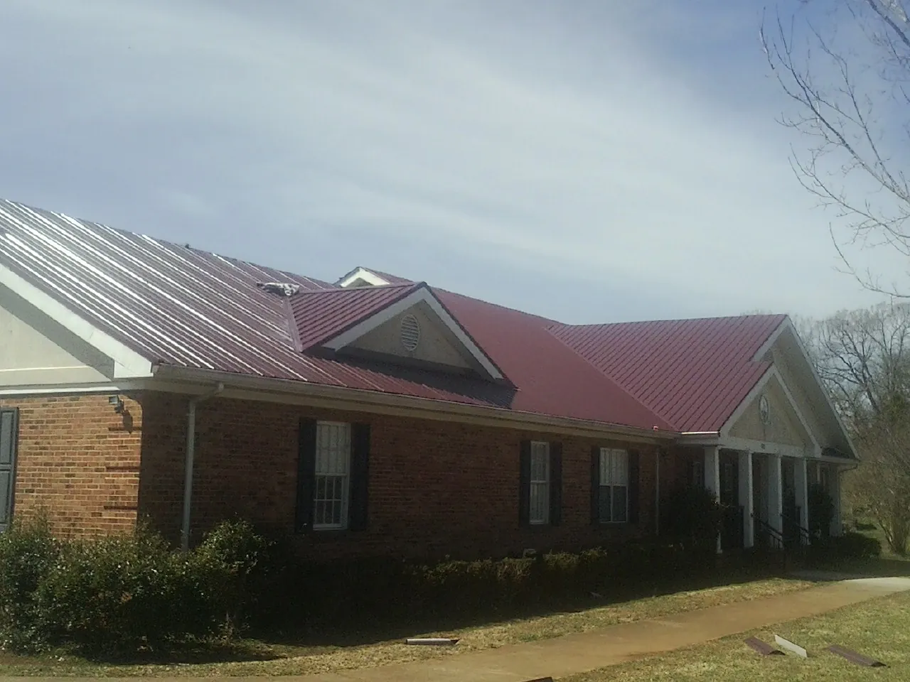 Red metal roof with gabled entries on a long brick building, from a Hail Damage Roof Repair job in Audubon