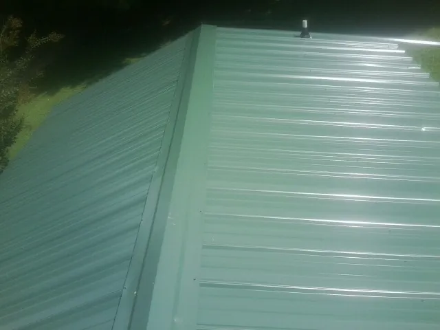 New green metal panels meeting at the ridge of a roof — Flat Roof Repair work by our crew in Audubon
