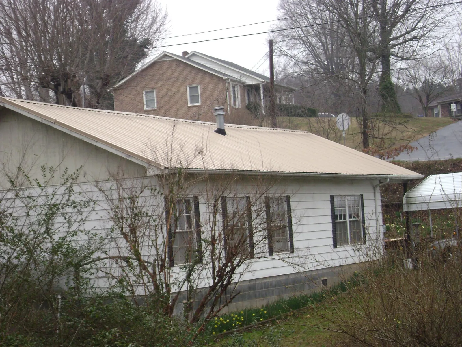 Tan metal roof on a white sided house set into a hillside — Commercial Roofing by Roofing Brothers in Audubon